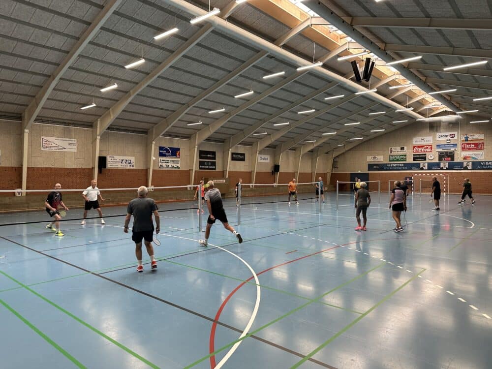 Badmintonspillere i aktion i Elbohallens idrætssal – ideel til leje af lokaler i Fredericia til sport og motion. Kontakt os for leje af lokaler eller baner